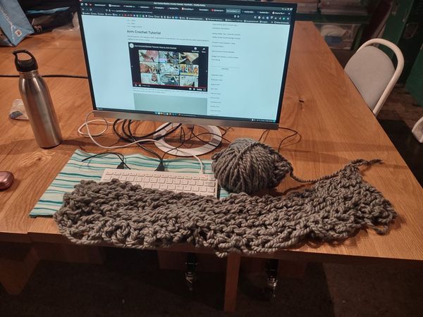 A crochet project and ball of gray yarn laid out in front of a computer open to "Arm crochet tutorial"